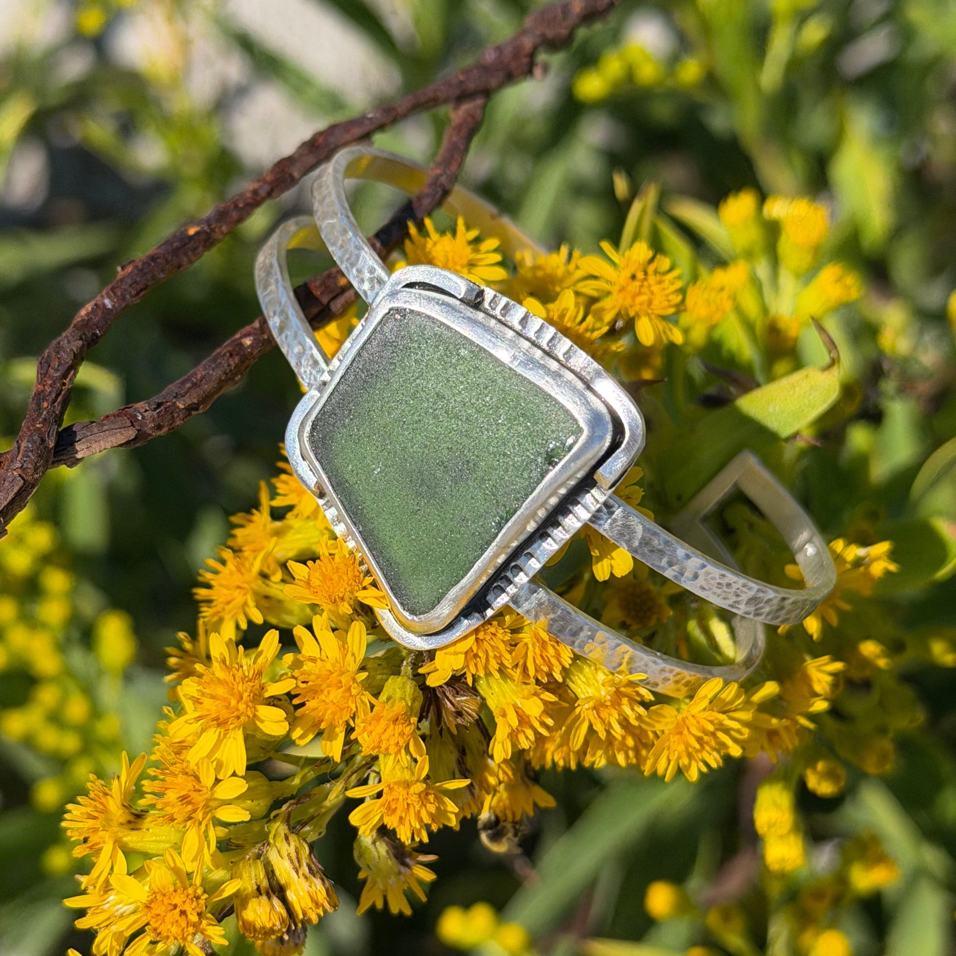 Silver ring with a green stone on a branch with yellow flowers