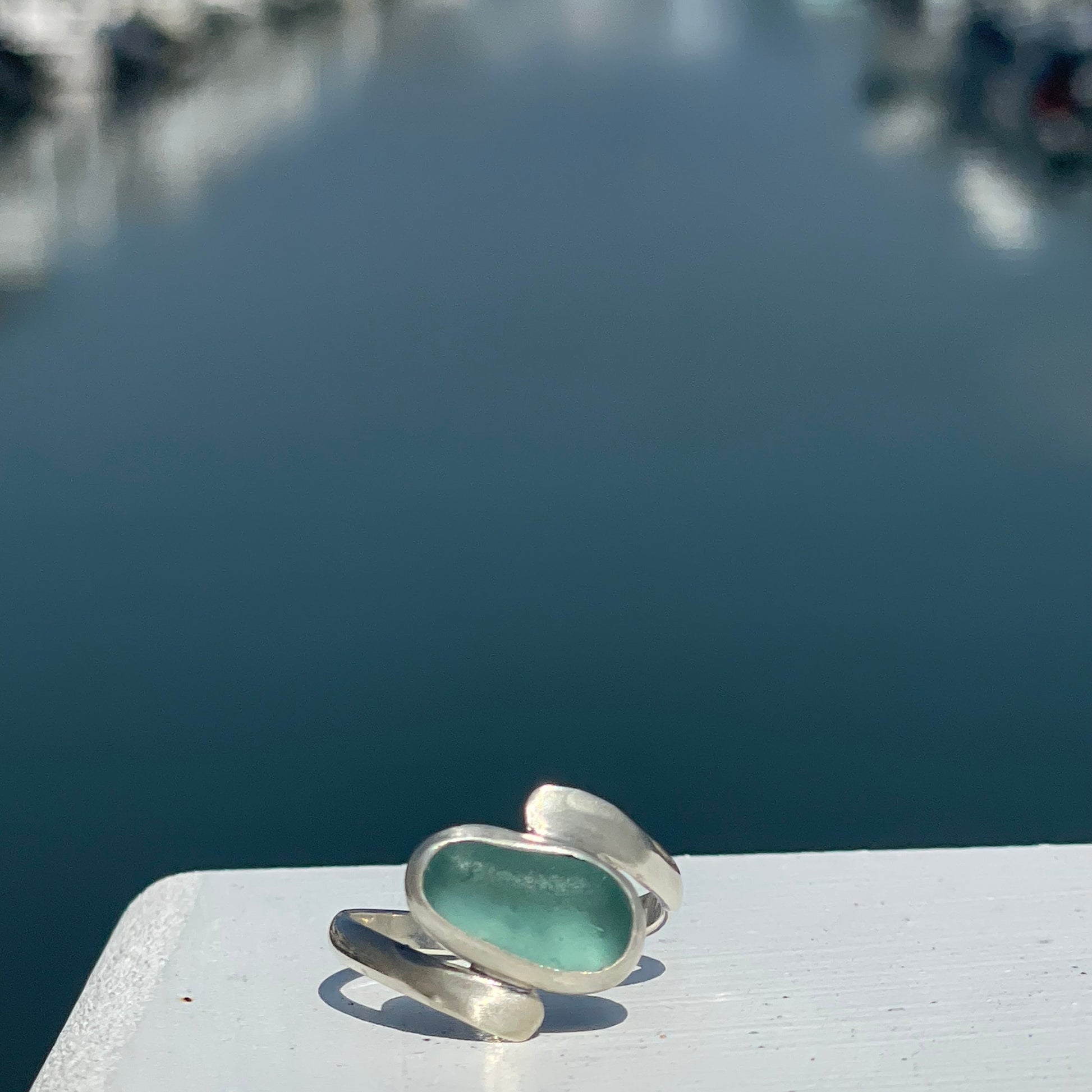 Teal ring with silver band on a white surface against a blurred background